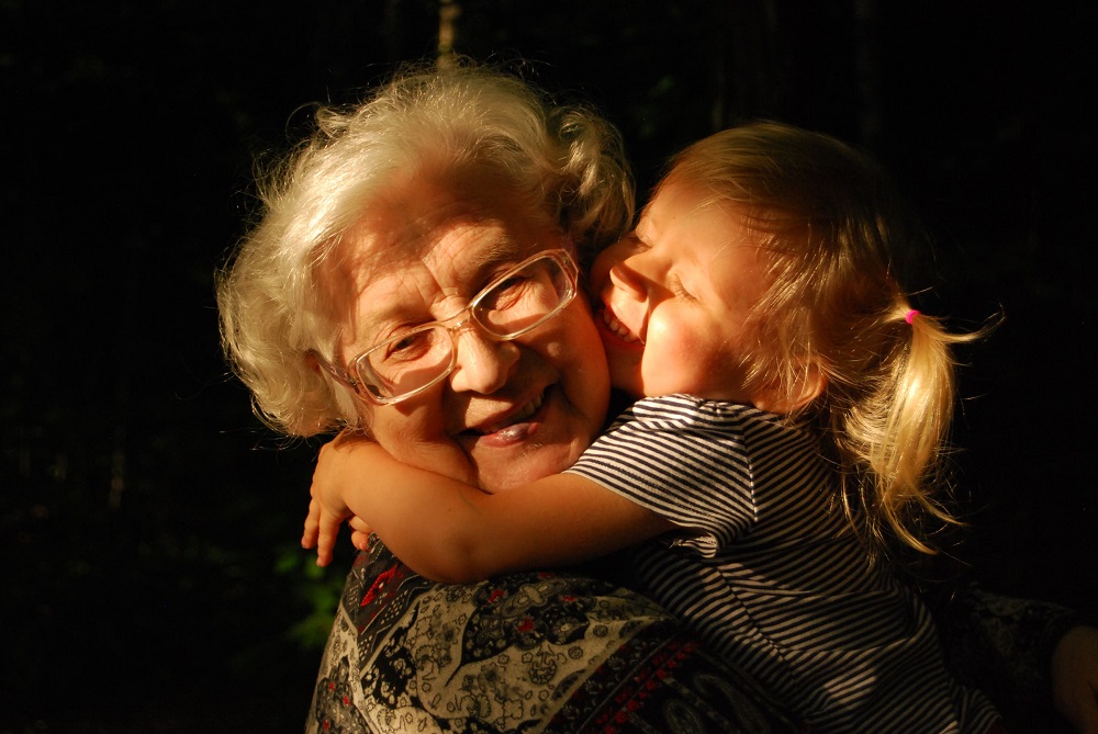 A grandchild joyfully hugs her grandmother's neck