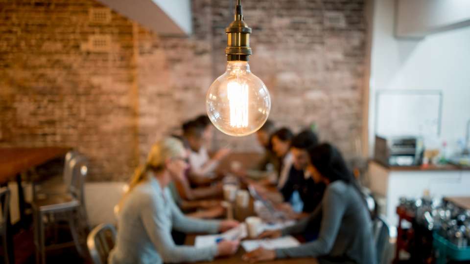image of group of people at table discussing with a light bulb overhead